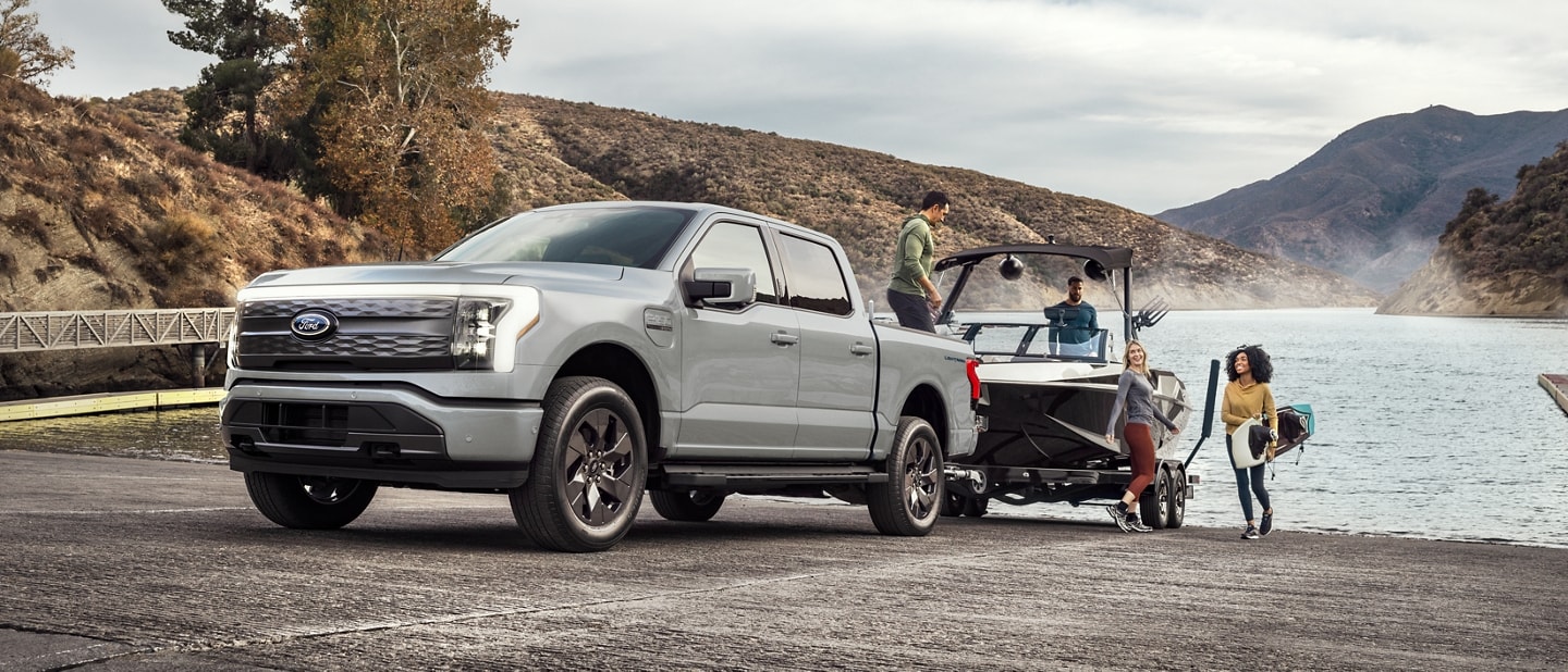 2023 Ford F-150® Lightning® hitched to a boat on a lake boat launch with people unloading gear