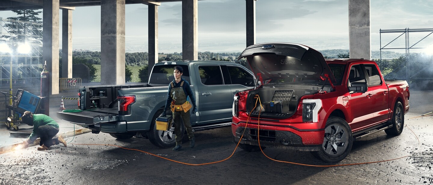 Two 2023 Ford F-150® Lightning® trucks at a construction site with a man using Pro Power Onboard