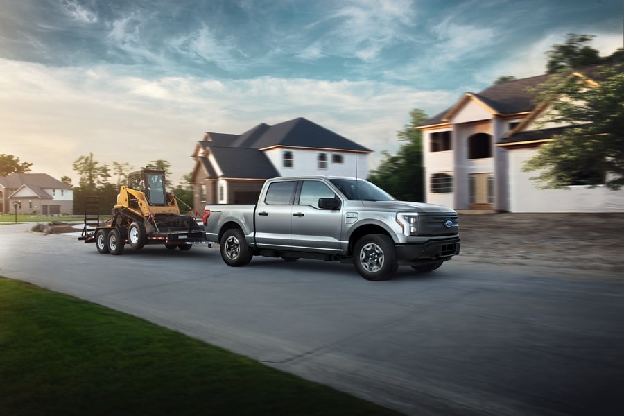 2023 Ford F-150® Lightning® pulling a backhoe on a trailer in a new subdivision