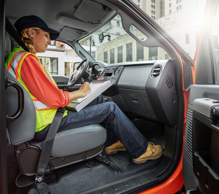 Worker writing on clipboard in passenger seat of 2023 Ford F-750 Crew Cab in Tangier Orange