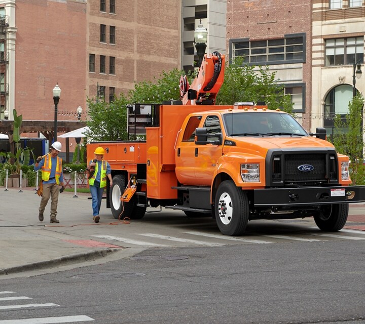 Workers walking near 2023 Ford F-750 Crew Cab in Tangier Orange with aerial lift upfit