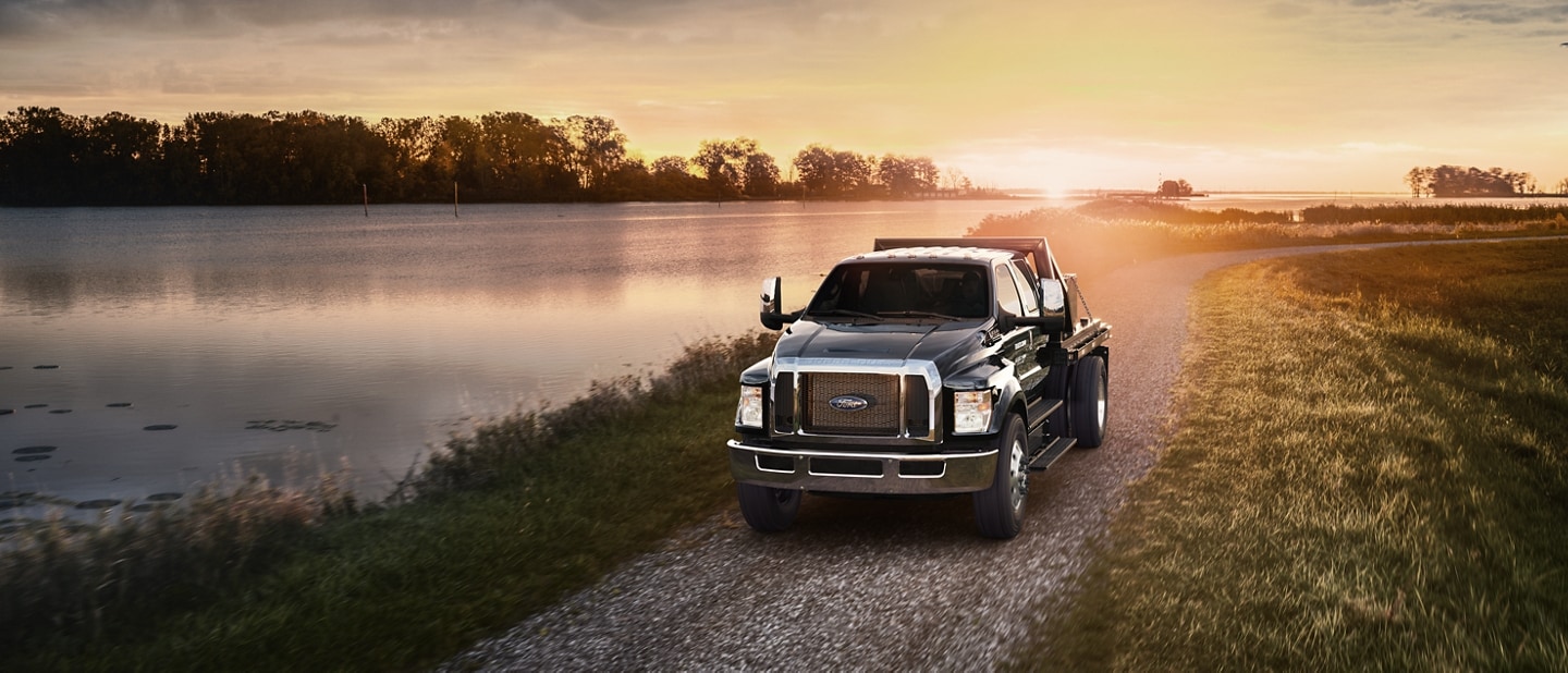 2024 Ford F-750 Crew Cab in Agate Black with utility stake bed upfit being driven near a lake