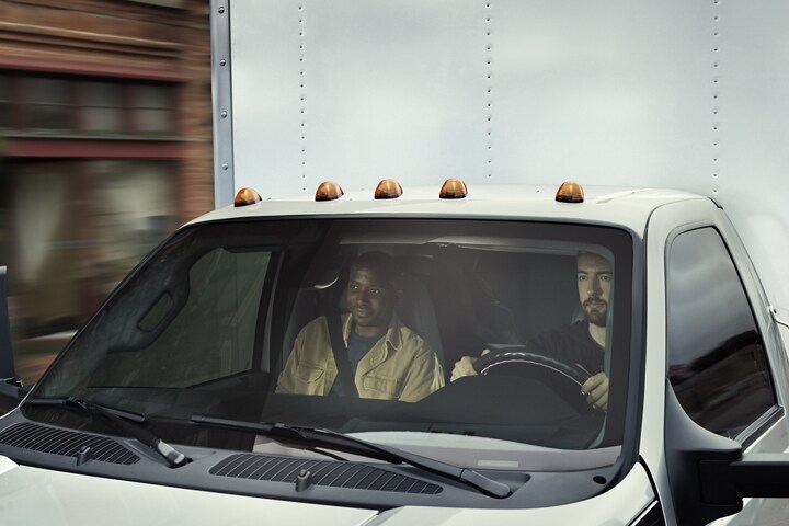 Close-up of a driver and passenger behind windshield of 2024 Ford F-750 Regular Cab with box truck upfit in Ingot Silver