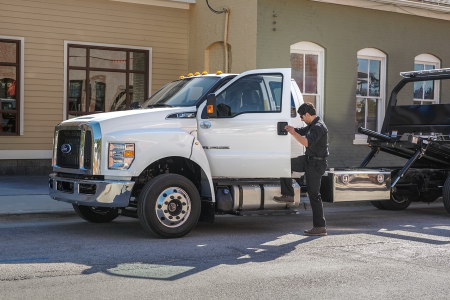 Person entering 2024 Ford F-650 SuperCab with rollback body flat bed and tow truck in Oxford White