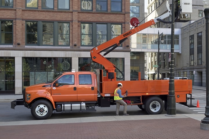 Worker fixing streetlight on city street while inside aerial lift upfit on 2024 Ford F-750 Crew Cab in Tangier Orange