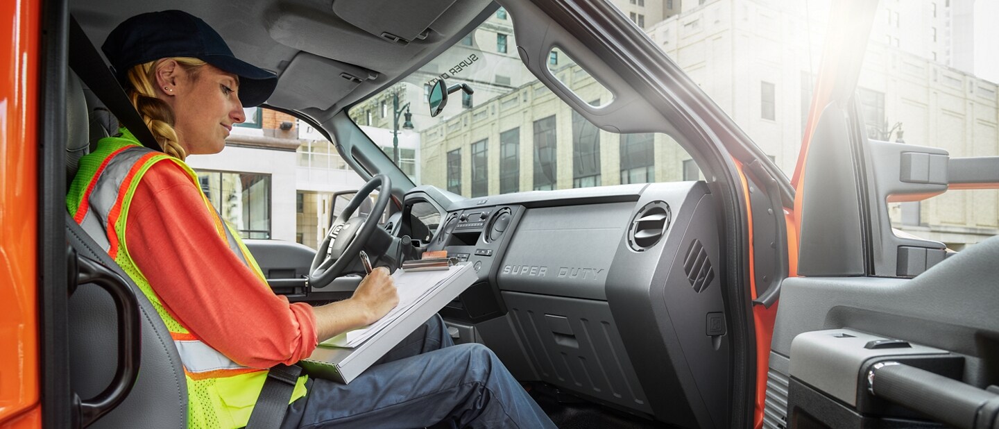 Worker writing on clipboard in passenger seat of 2024 Ford F-750 Crew Cab in Tangier Orange