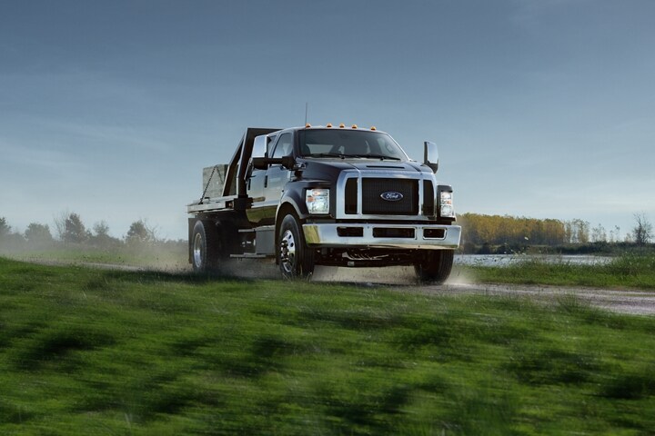 2025 Ford F-750 with utility stake bed upfit in Agate Black being driven on dirt road near grass and water