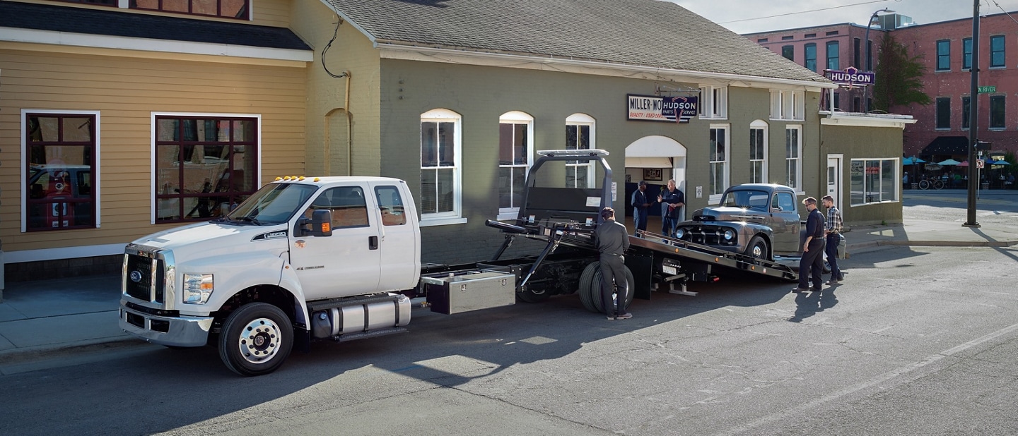 2026 Ford F-650® shown in Oxford White with rollback body flatbed loading a pickup truck into the bed