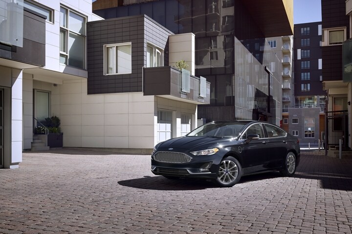 Fusion plug in hybrid titanium in agate black parked in front of a modern apartment complex