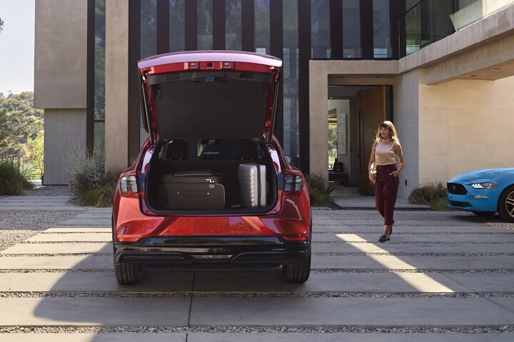 Rear end of the 2023 Ford Mustang Mach-E® parked in a driveway with a legacy Ford Mustang parked to the right