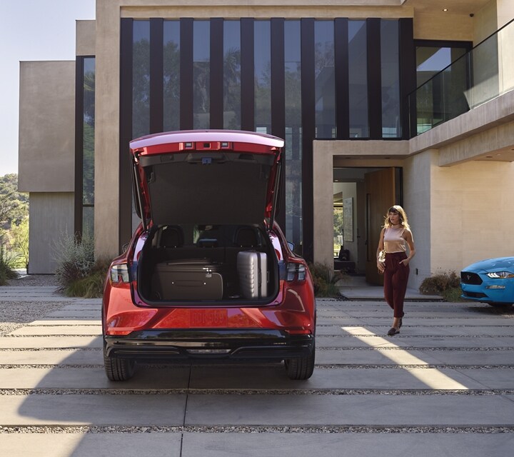 Rear end of the 2023 Ford Mustang Mach-E® SUV parked in a driveway with a legacy Ford Mustang parked to the right