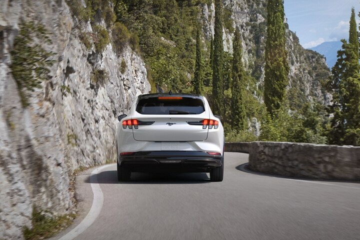 Rear view of a 2023 Ford Mustang Mach-E® SUV being driven on a scenic mountain highway