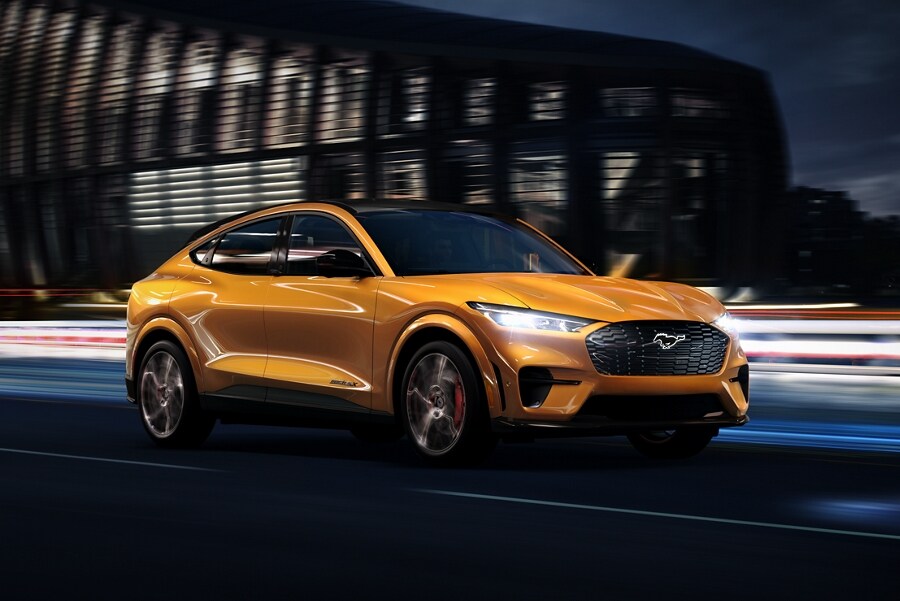 Cyber Orange Metallic 2023 Ford Mustang Mach-E® being driven on a highway past a stadium at night