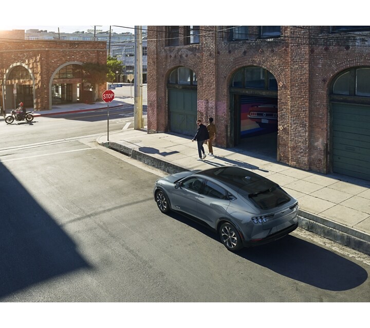 Woman walking with man who looks back at a 2023 Ford Mustang Mach-E SUV parked on a city street