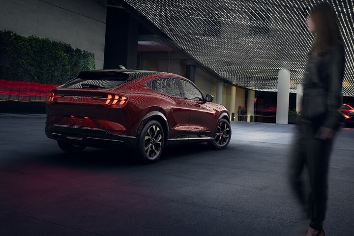 Blurry woman looking at a rear view of the 2023 Ford Mustang Mach-E® at night under moody outdoor lighting