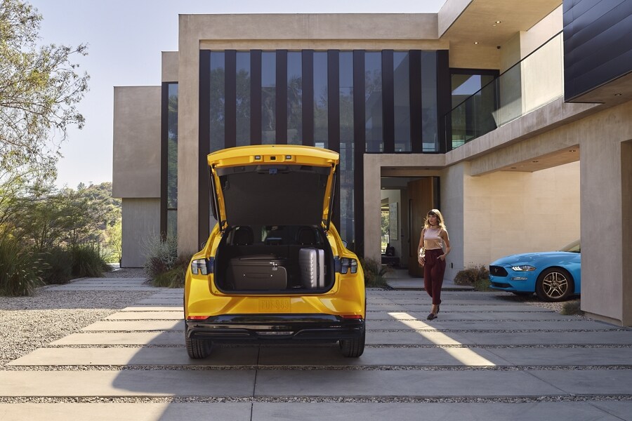 2023 Ford Mustang Mach-E® with open cargo hatch parked in the driveway of a luxury home