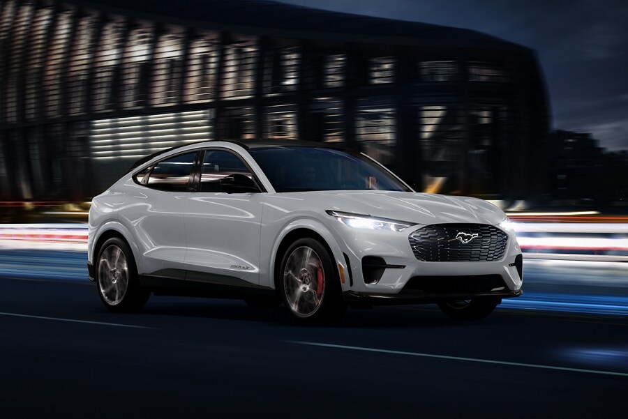 Space White Metallic 2023 Ford Mustang Mach-E® SUV being driven on a highway past a stadium at night
