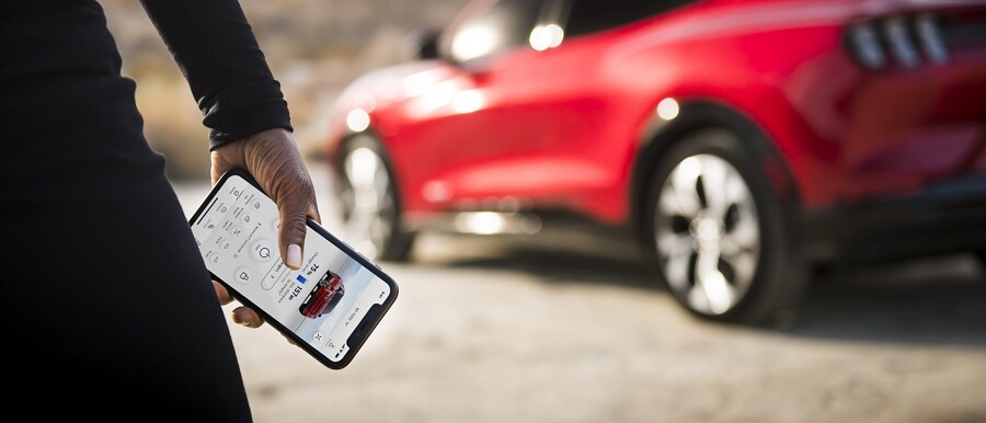 Person holding smartphone with a 2023 Ford Mustang Mach-E® in the background
