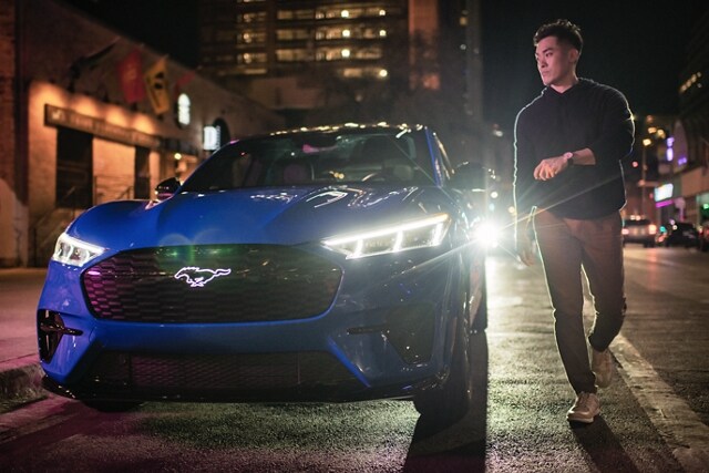 Man walking up to a 2023 Ford Mustang Mach-E® SUV with illuminated Pony graphic and headlights at night