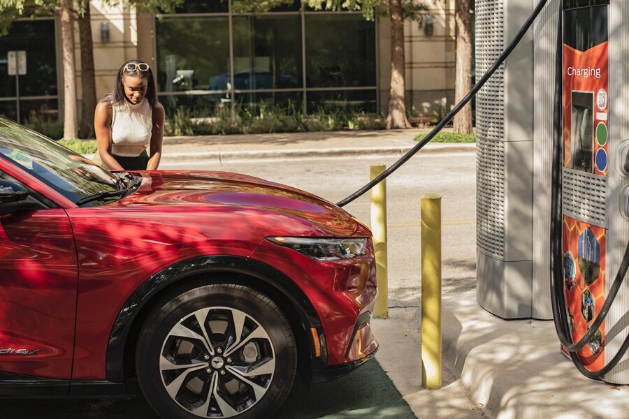 Woman setting a coffee on a 2023 Ford Mustang Mach-E® SUV at a charging station