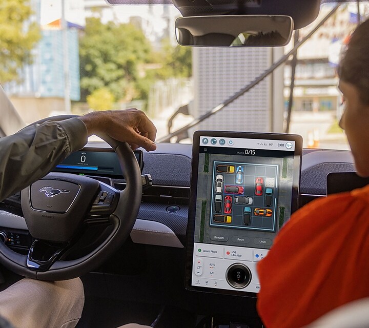 Two people inside a parked 2023 Ford Mustang Mach-E® SUV with a game on the portrait touchscreen right