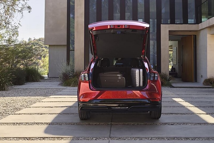 2024 Ford Mustang Mach-E® shown parked on a stone driveway with rear liftgate open and luggage inside