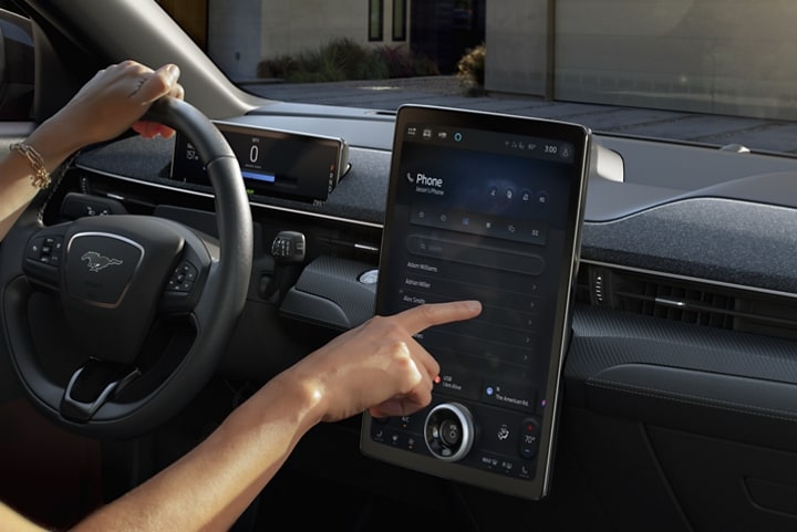 A woman sitting in the driver's seat using the in-vehicle touchscreen