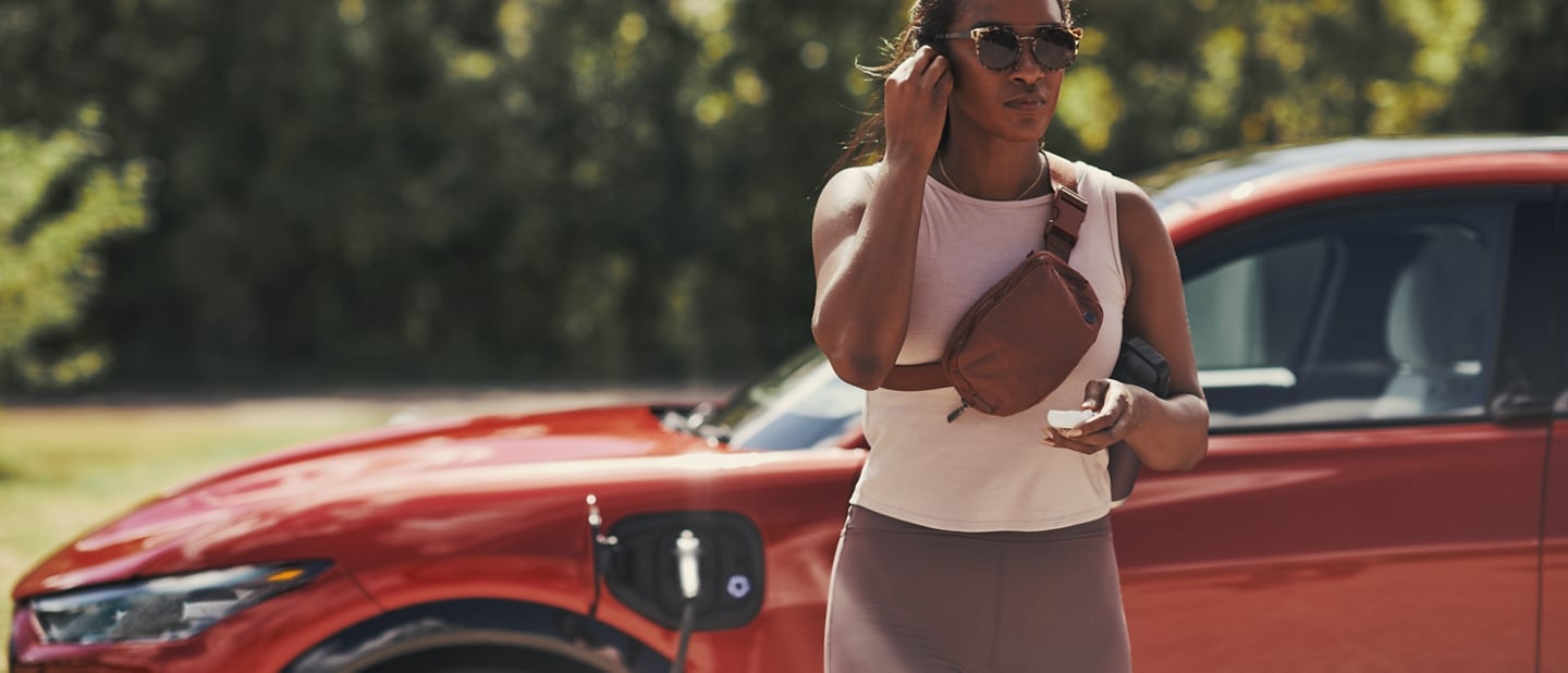 2024 Ford Mustang Mach-E® shown in profile with a woman standing outside the car while it's charging