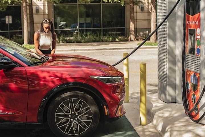 A woman standing outside her 2024 Ford Mustang Mach-E® using a public charging station