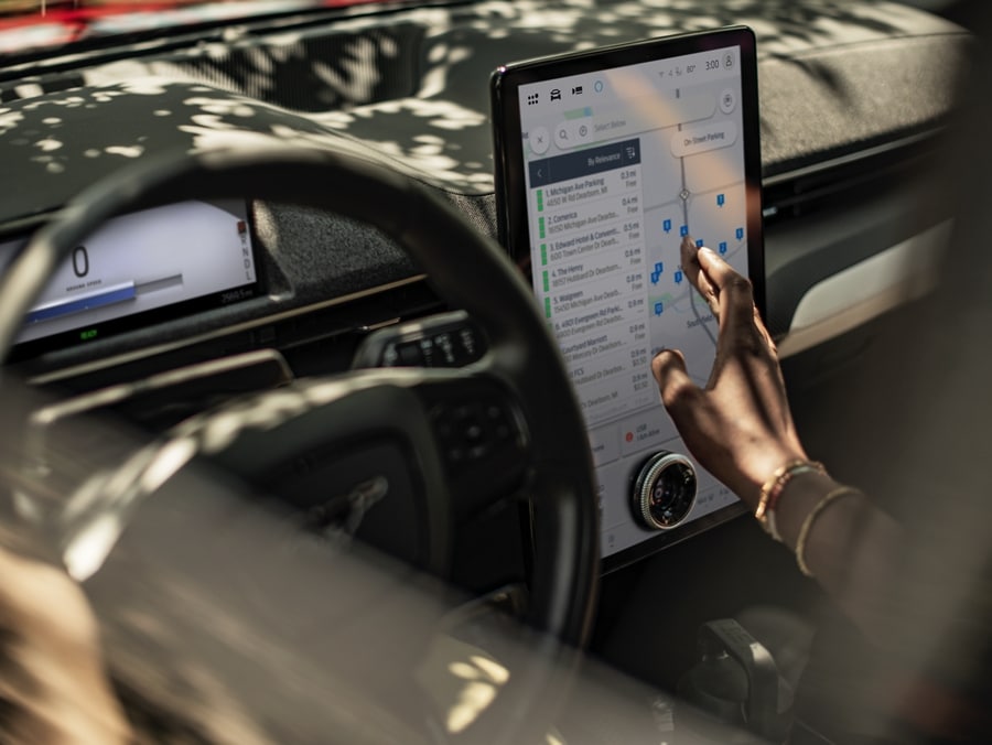 A person sitting inside the Ford Mustang Mach-E® using the touch screen to find charging locations on a map