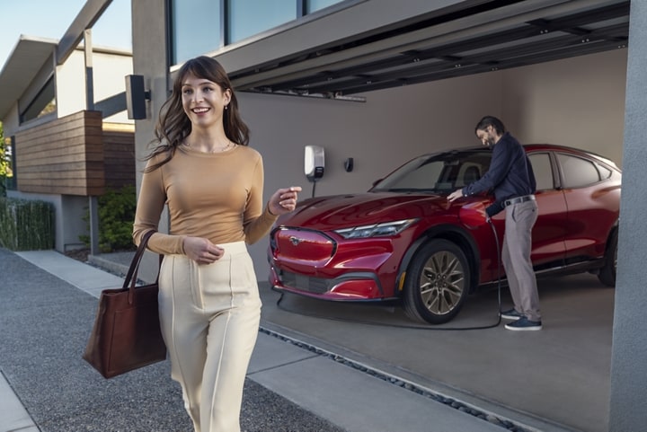 A man and woman standing outside the vehicle in front of a home charger