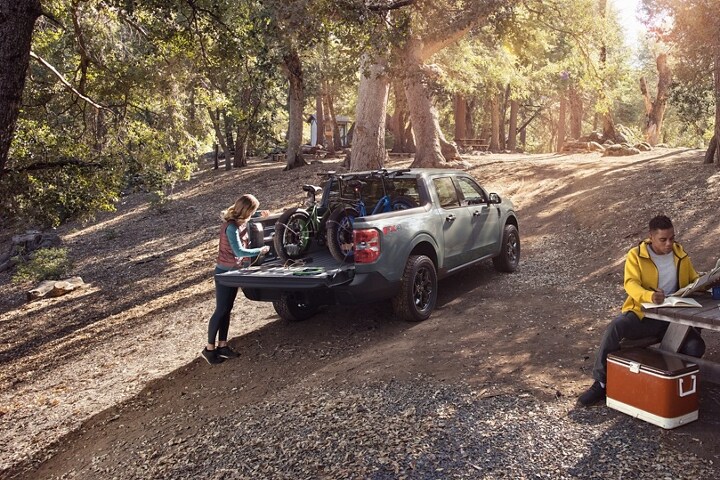 Woman at a campsite plugs an electric bike into the bed of a 2023 Ford Maverick® XLT truck