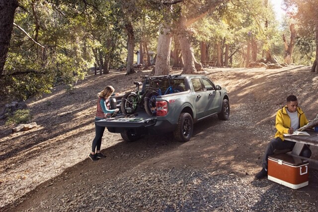 Woman at a campsite plugs a bike into the 400-watt 110V Outlet in the bed of a 2023 Ford Maverick® XLT truck