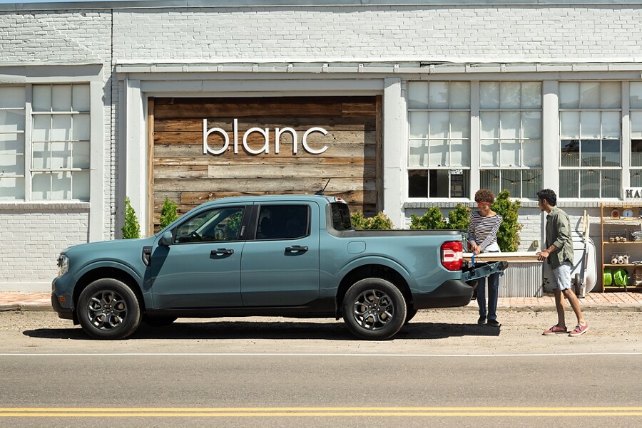 2 people load lumber into the bed of a 2023 Ford Maverick® truck outside a trendy home store called Blanc