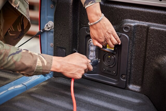Hand plugging an extension cord into the 400-watt 110V outlet in the bed of a 2023 Ford Maverick® truck