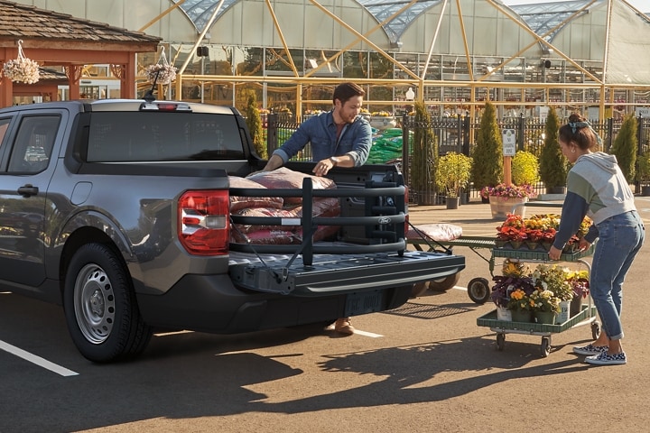 2 people putting flowers and bags of soil into the bed of a 2023 Ford Maverick® truck with available bed extender