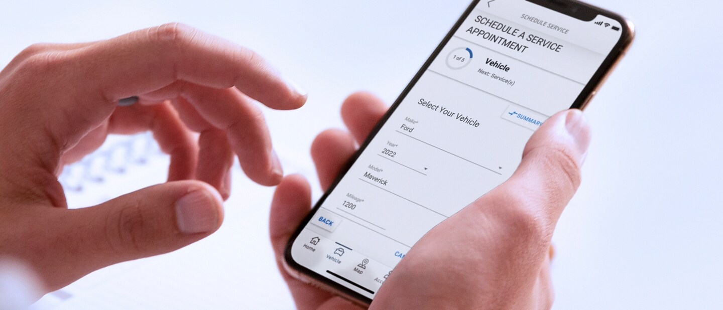 A hand holds a smartphone displaying the Schedule Service menu in the FordPass® App