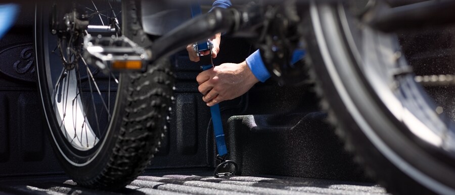 Close-up of the interior of a truck bed of a 2024 Ford Maverick® truck with a person's arm securing a dirt bike