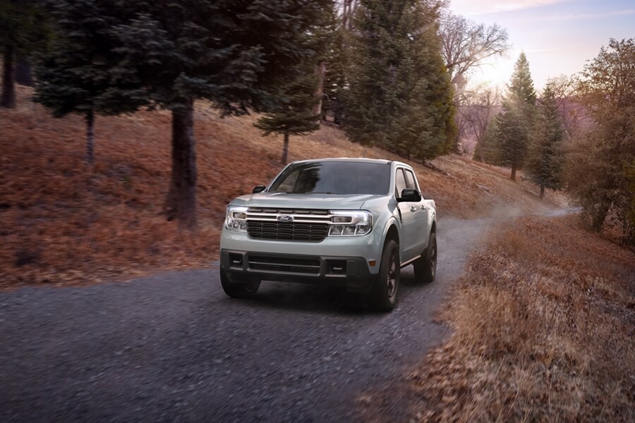 A 2024 Ford Maverick® in Azure Grey Metallic is being driven on a tree-lined scenic location