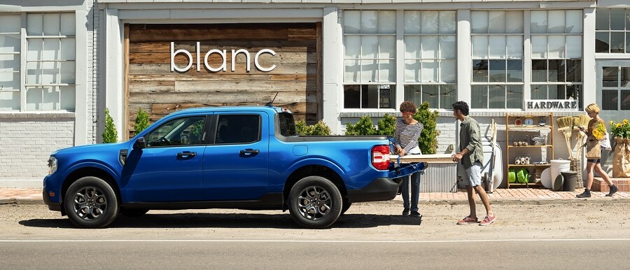A 2024 Ford Maverick® truck in Atlas Blue Metallic is parked in the grass in a scenic location with cargo in the tailgate