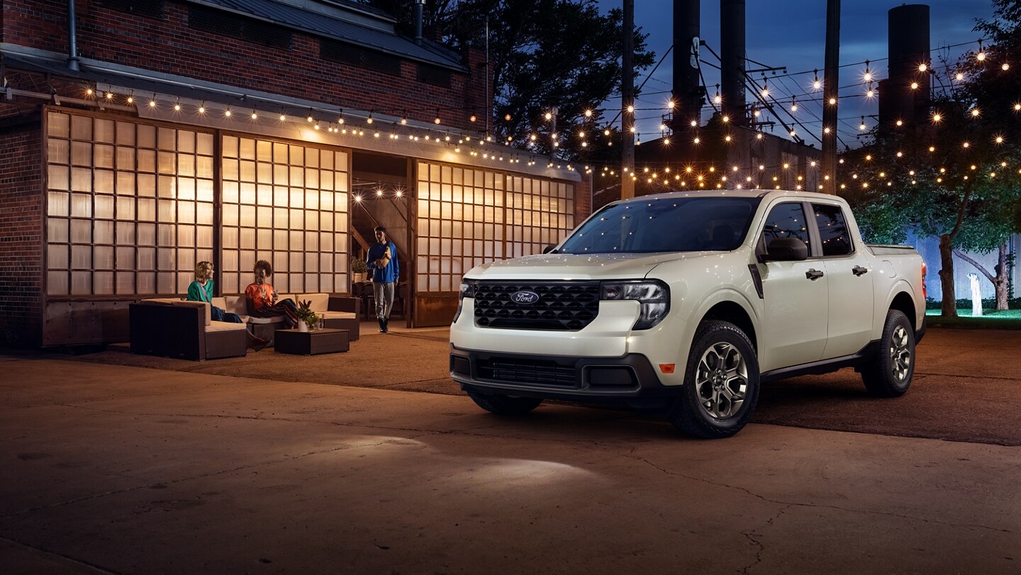A white 2025 Ford Maverick® pickup parked in the forecourt of a restaurant at night