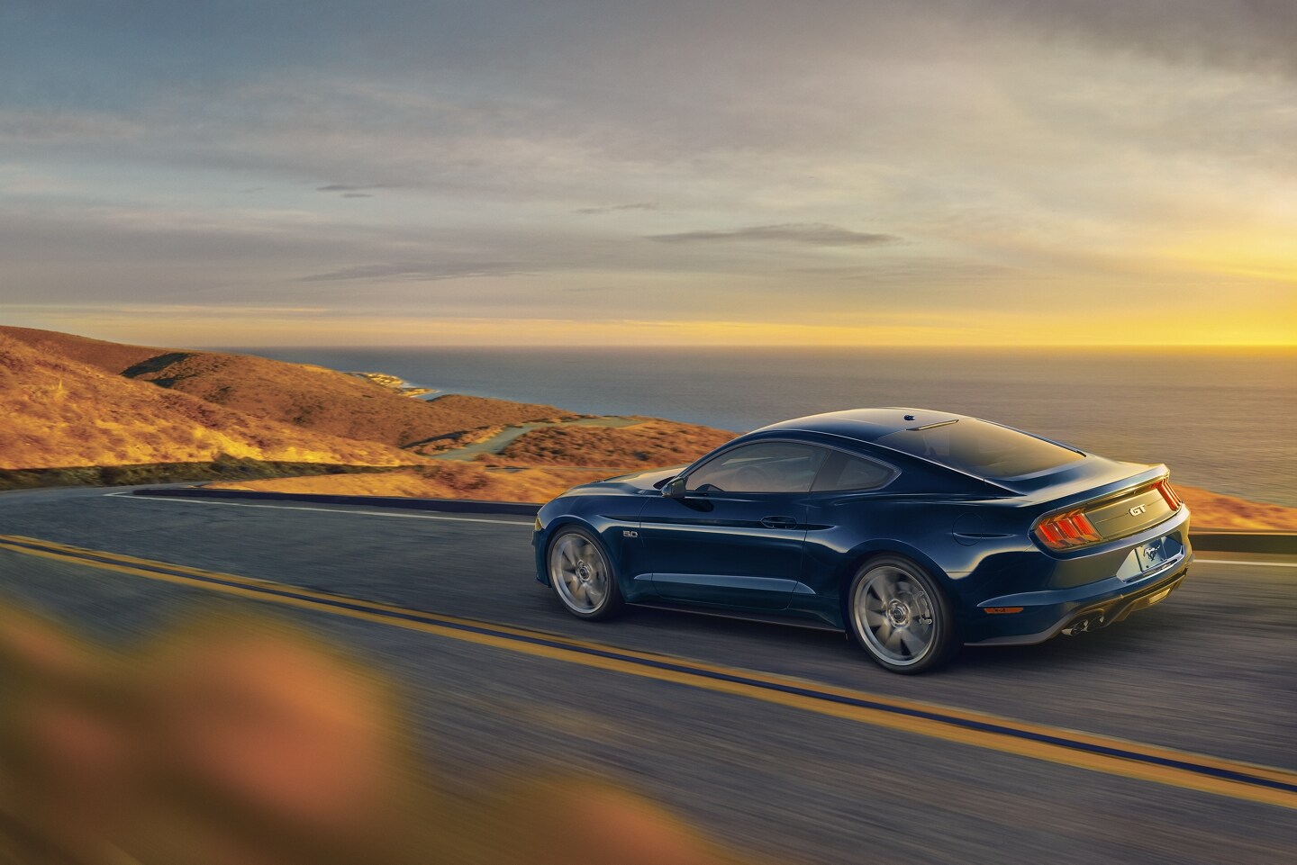 2021 Ford Mustang in Antimatter Blue being driven on the open road with an ocean in the background