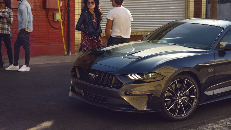 2023 Ford Mustang® coupe in Carbonized Grey Metallic parked on the street with four people standing nearby