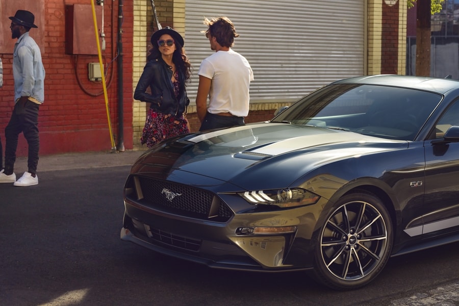 2023 Ford Mustang® coupe in Carbonized Grey Metallic parked on the street with four people standing nearby