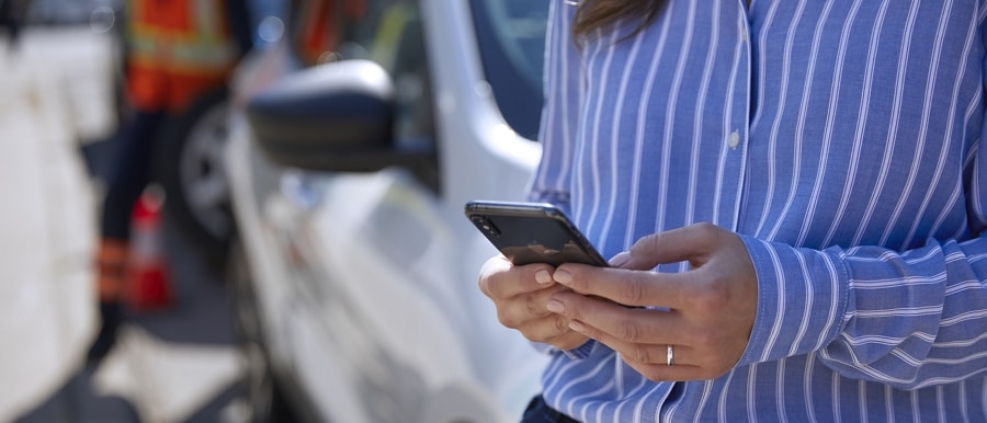 Person uses a smartphone while a technician repairs a tire on their vehicle