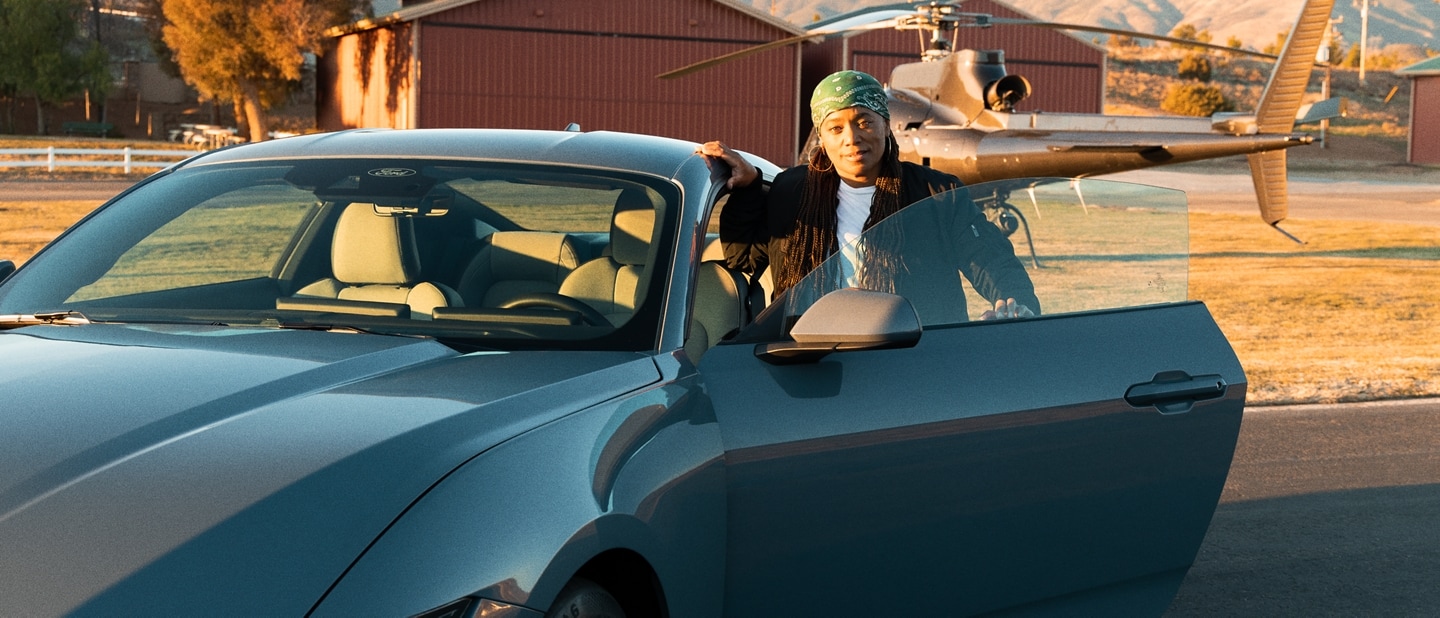 Dee Bryant standing near the open driver-side door of a parked 2024 Ford Mustang® coupe