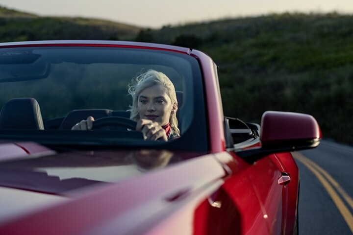 Person driving a 2024 Ford Mustang® convertible model in Rapid Red Metallic Tinted Clearcoat (extra-cost paint) on a highway
