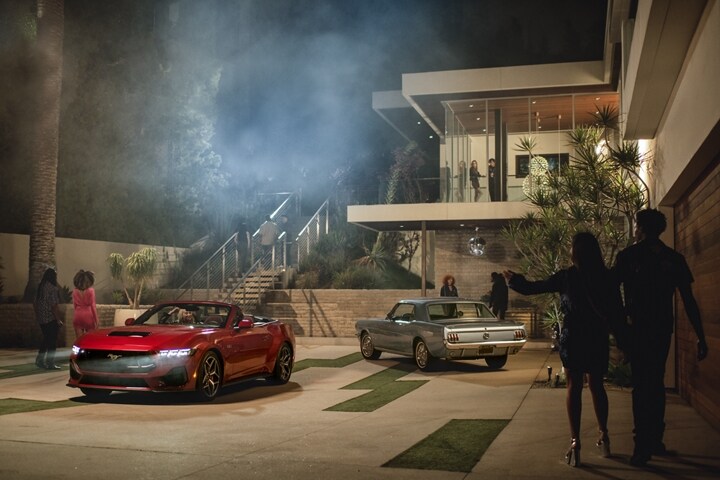 2024 Ford Mustang® GT convertible in Rapid Red Metallic Tinted Clearcoat (extra-cost paint) and first-gen Mustang® model by people