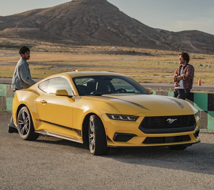 2024 Ford Mustang® EcoBoost® model with available Wheel and Stripe package parked on a racecourse near people