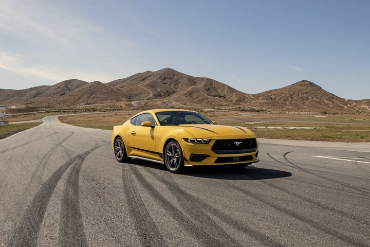 2024 Ford Mustang® EcoBoost® coupe in Yellow Splash Metallic Tri-coat (extra-cost paint) parked on a racecourse